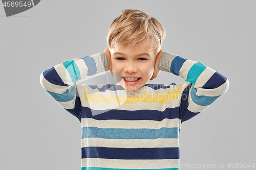 Image of stressed boy in pullover closing ears by hands