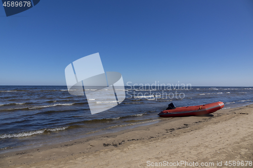 Image of Rubber boat on a sand seashore on a blue sky background.