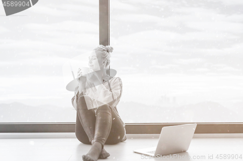 Image of woman drinking coffee and using laptop at home