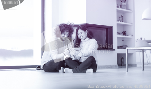 Image of multiethnic couple using tablet computer in front of fireplace