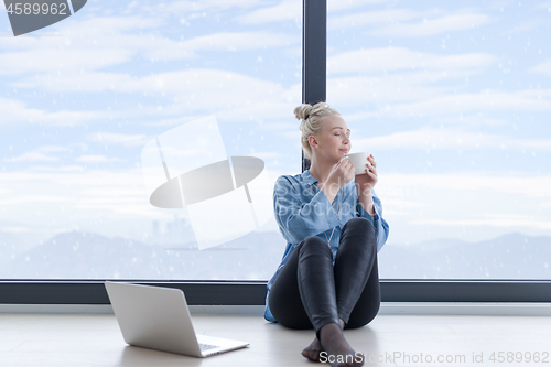 Image of woman drinking coffee and using laptop at home