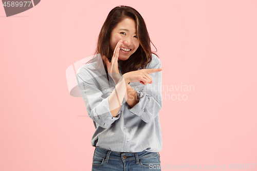 Image of The young woman whispering a secret behind her hand over pink background