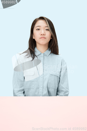 Image of The serious business woman sitting and looking at camera against blue background.