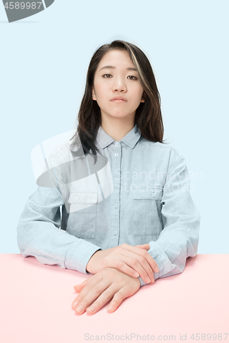 Image of The serious business woman sitting and looking at camera against blue background.