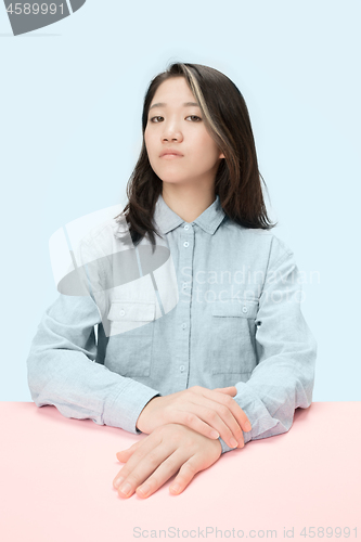 Image of The serious business woman sitting and looking at camera against blue background.