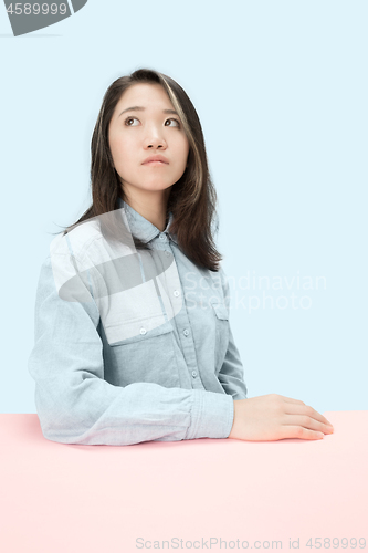 Image of The serious business woman sitting and looking up against blue background.