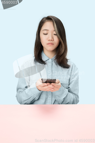 Image of The serious business woman sitting and looking at phone against blue background.