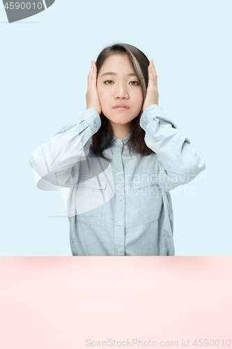 Image of portrait of stressed woman sitting at table with closed and covering her ears with hands.