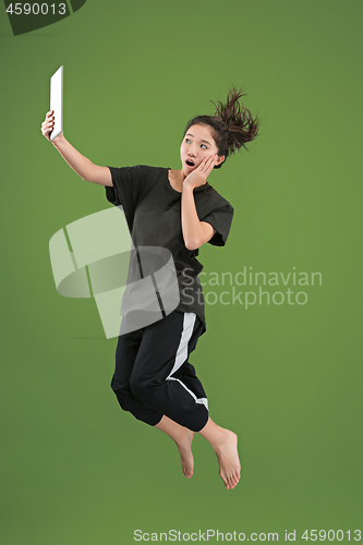 Image of Image of young woman over green background using laptop computer or tablet gadget while jumping.