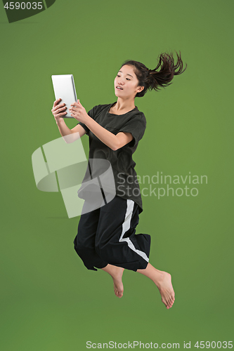 Image of Image of young woman over green background using laptop computer or tablet gadget while jumping.