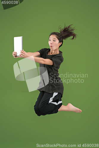 Image of Image of young woman over green background using laptop computer or tablet gadget while jumping.