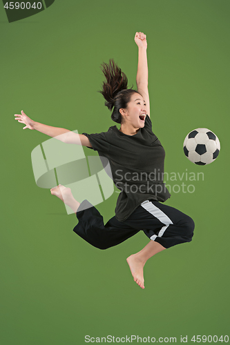 Image of Forward to the victory.The young woman as soccer football player jumping and kicking the ball at studio on green