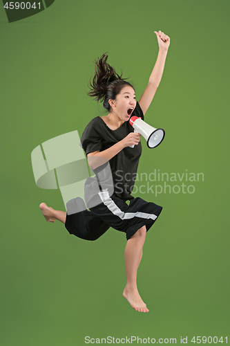 Image of Beautiful young woman jumping with megaphone isolated over green background