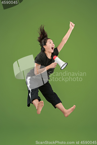 Image of Beautiful young woman jumping with megaphone isolated over green background