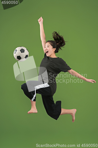 Image of Forward to the victory.The young woman as soccer football player jumping and kicking the ball at studio on green