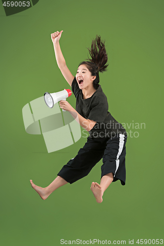 Image of Beautiful young woman jumping with megaphone isolated over green background