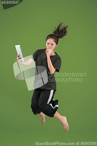 Image of Image of young woman over green background using laptop computer or tablet gadget while jumping.