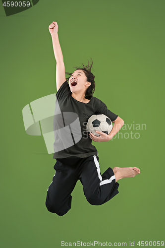 Image of Forward to the victory.The young woman as soccer football player jumping and kicking the ball at studio on green