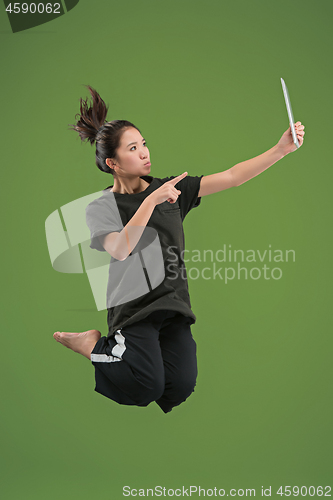 Image of Image of young woman over green background using laptop computer or tablet gadget while jumping.