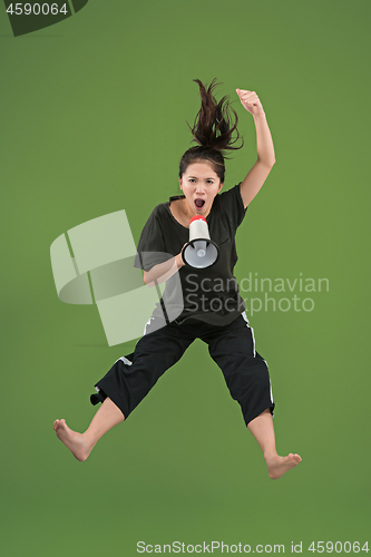 Image of Beautiful young woman jumping with megaphone isolated over green background