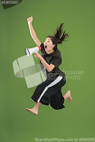 Image of Beautiful young woman jumping with megaphone isolated over green background