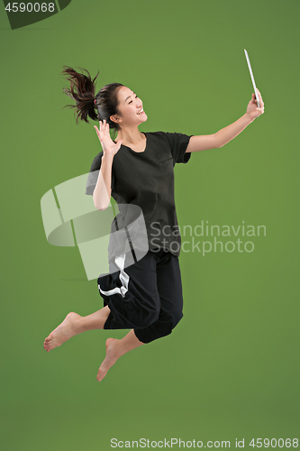 Image of Image of young woman over green background using laptop computer or tablet gadget while jumping.