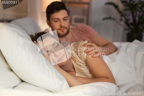 Image of man waking his sleeping wife up in bed at home