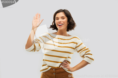 Image of smiling woman in striped pullover waving hand