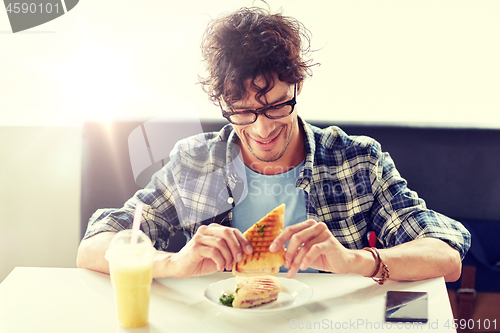 Image of happy man eating sandwich at cafe for lunch