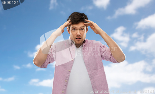 Image of man touching his head over blue sky background