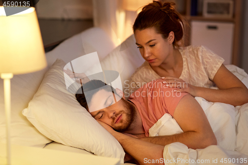 Image of woman wakes her sleeping husband up in bed at home