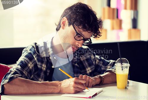 Image of man with notebook and juice writing at cafe