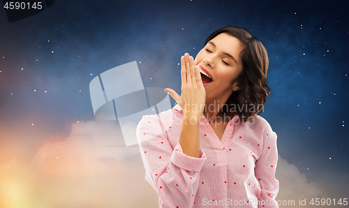 Image of sleepy woman in pajama yawning over night sky