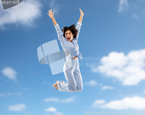 Image of happy woman in pajama jumping over blue sky
