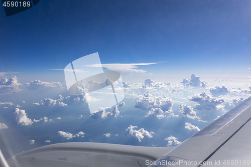 Image of Airplane wing above fluffy white clouds in a blue sky.