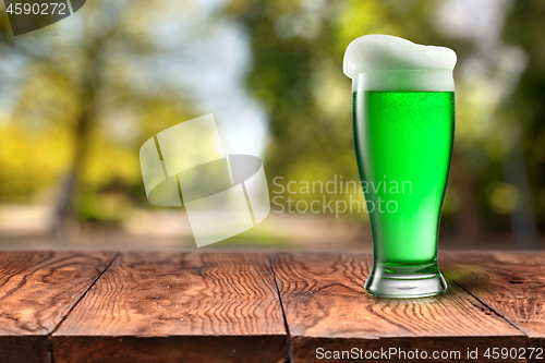 Image of Green beer in glass on wooden table against blurred park.