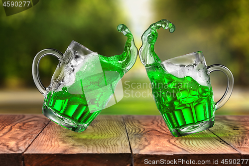 Image of Splashes of fresh green beer in two jumping glasses.