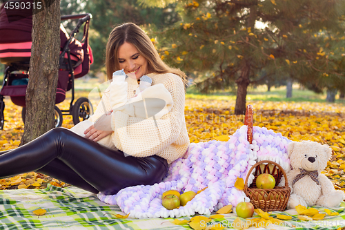 Image of Mom with newborn baby on a picnic in the autumn park, next to stands a stroller