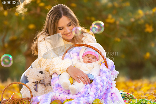 Image of Mom happily looks at the two-month-old baby sleeping in a basket, flying soap bubbles