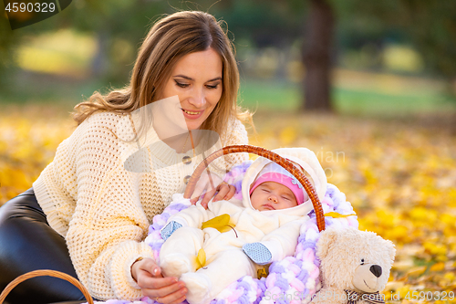 Image of Mom put the child in a basket and crouched next to her, resting in the park