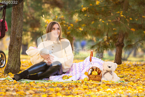 Image of Mom sits on a picnic in the autumn park, holding a newborn baby in her arms