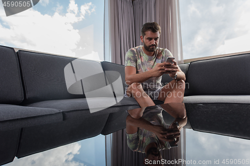 Image of young casual man using a mobile phone at home