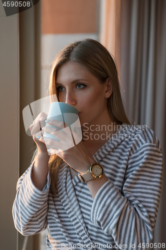 Image of young woman enjoying evening coffee by the window
