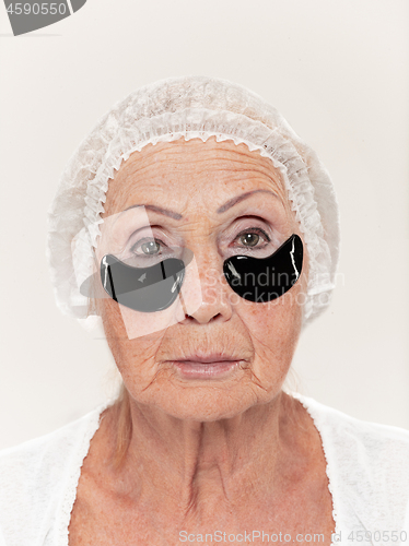 Image of Senior woman at studio isolated on white wall looking at camera and making masks under eyes