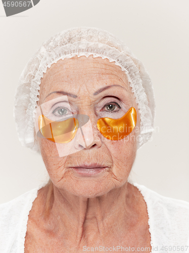 Image of Senior woman studio isolated on white wall beauty concept looking at camera making masks under eyes