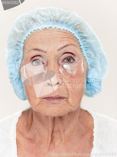 Image of Senior woman studio isolated on white wall beauty concept looking at camera making masks under eyes