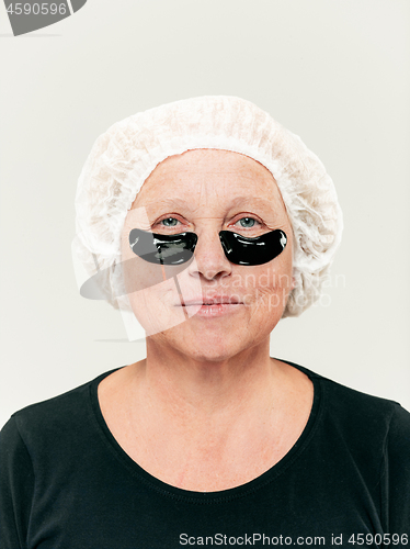 Image of Senior woman studio looking at camera making masks under eyes