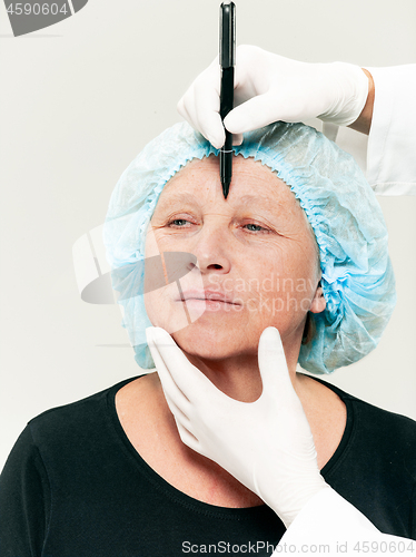 Image of surgeon doing skin check on mid age woman before plastic surgery