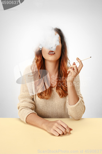 Image of Tranquil woman sitting and smoking resting at the table. Cloud of smoke covering her face. Copy space