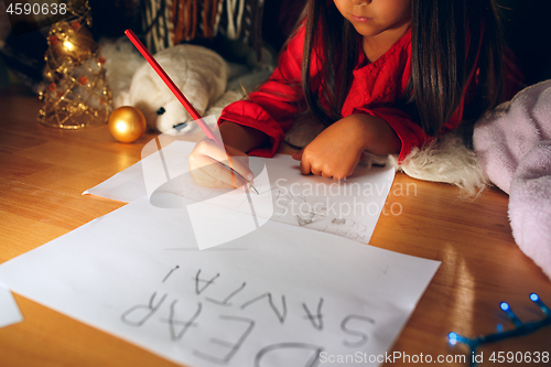 Image of Merry Christmas and Happy Holidays. Cute little child girl writes the letter to Santa Claus near Christmas tree